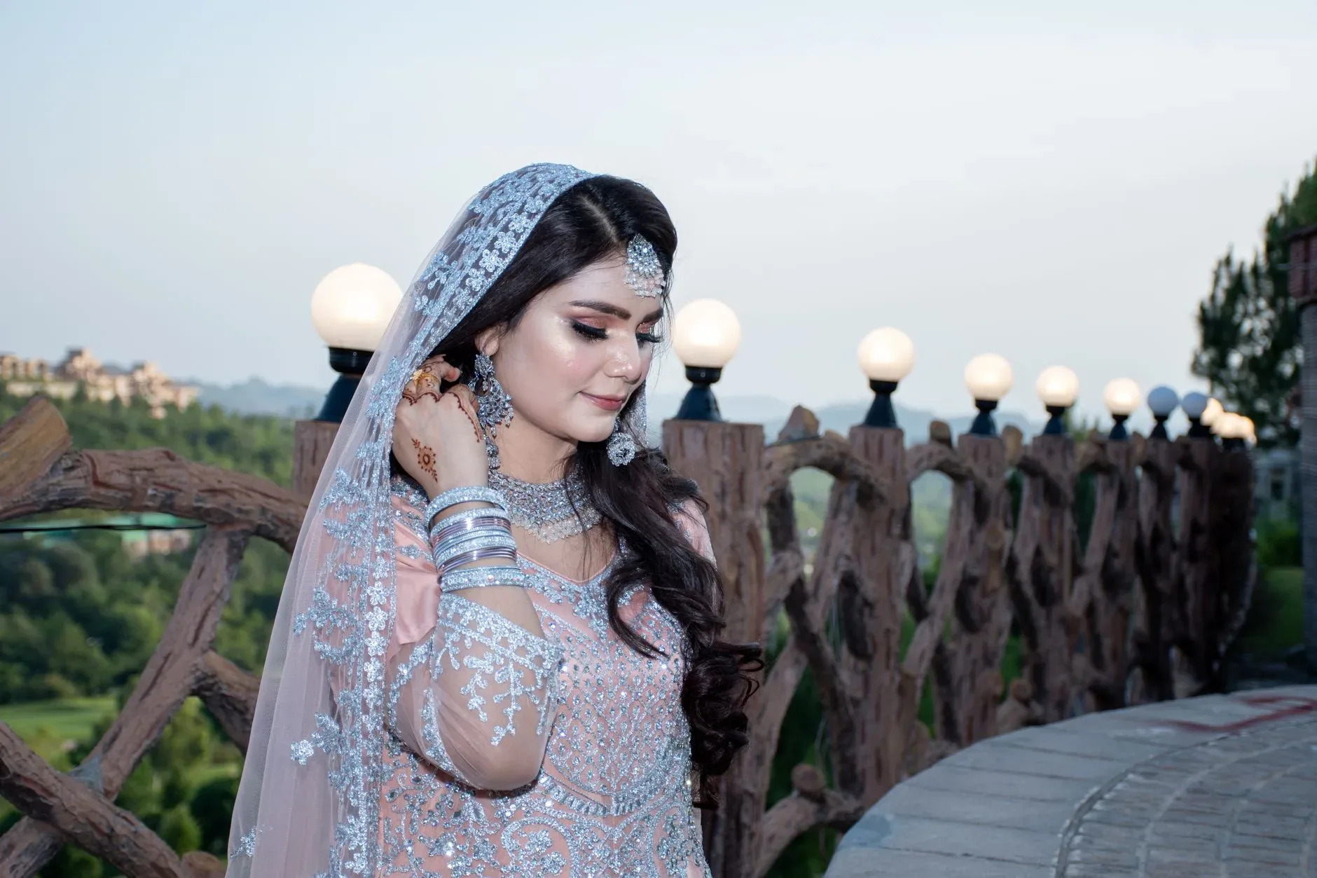 A bride in traditional Pakistani bridal attire smiling outdoors, showcasing elegance.